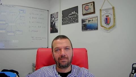 Immagine Alessandro Rossi, tecnico informatico dell’Ente, è seduto alla scrivania del suo ufficio. Indossa una camicia bianca a righe grigie.