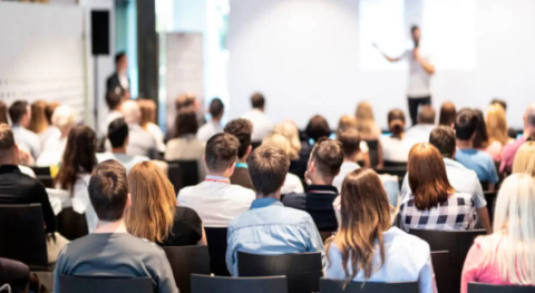 Un gruppo di persone partecipa a un seminario, seduto e attento durante la presentazione.
